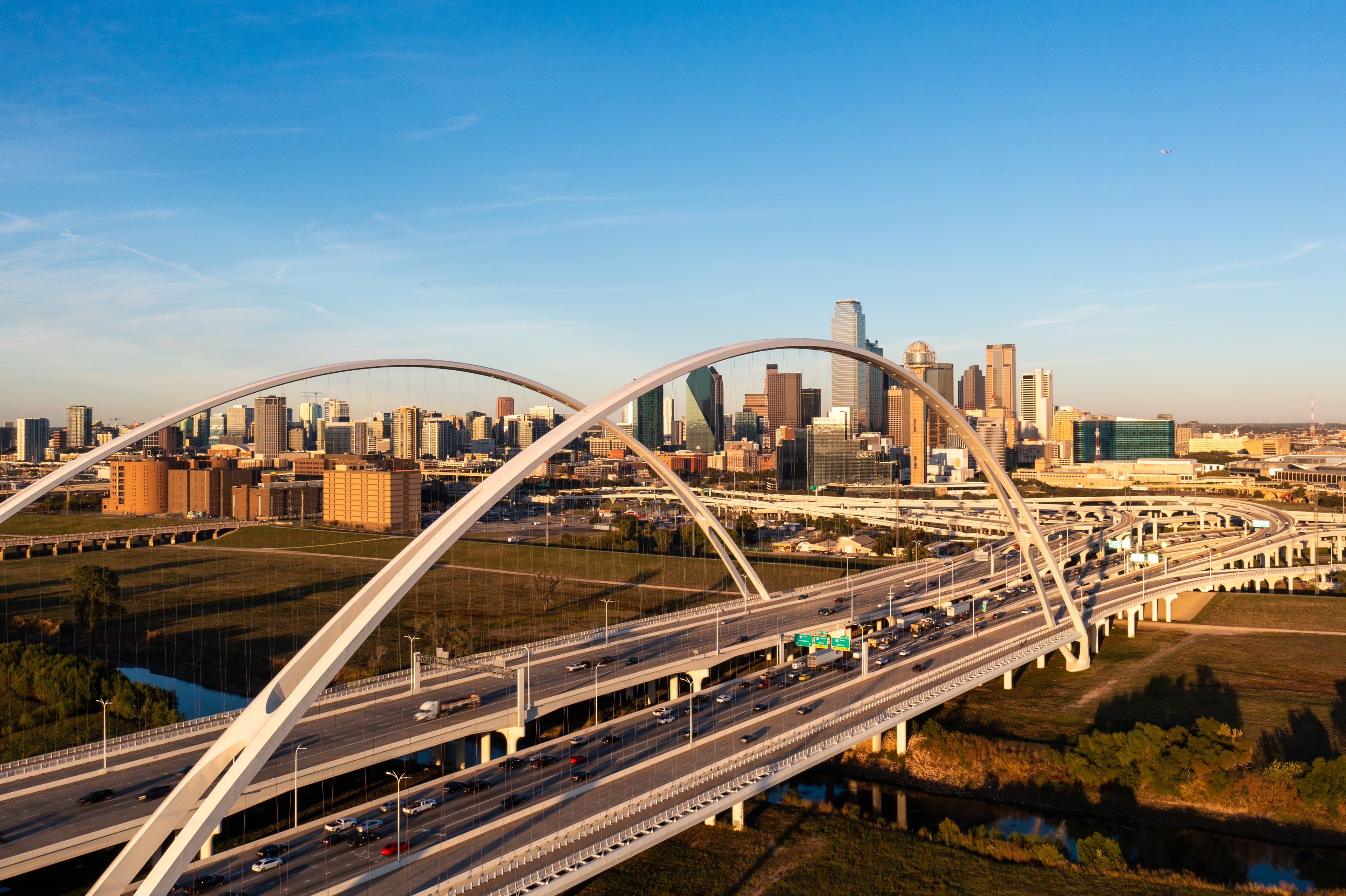 Dallas skyline at sunset behind the Margaret McDermott Bridge arches over I-30