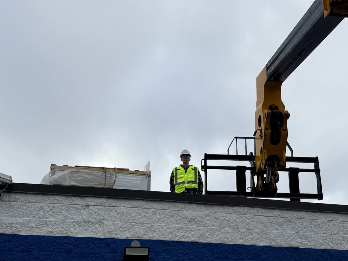 Technician on a rooftop guiding a crane spreader bar into position