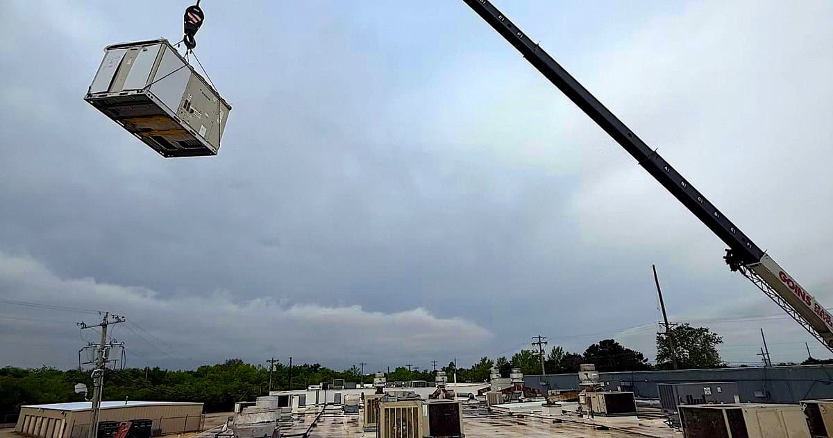 Rooftop unit hoisted by crane against an open sky